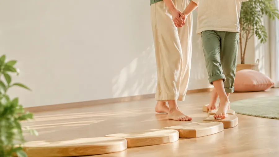 Kind und erwachsene Begleitperson bei einer Balanceübung auf hölzernen Trittsteinen